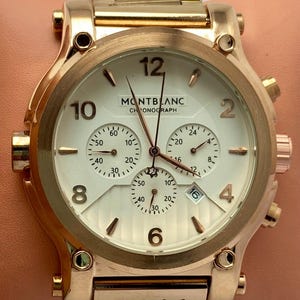 以下が含まれることがあります： MONTBLANC CHRONOGRAPHの文字が入った白い文字盤のローズゴールドトーンのクロノグラフ腕時計。メタリック仕上げで、2、4、6、8、10、12の数字、3つのサブダイヤル、4と5の間に日付表示窓を備えています。