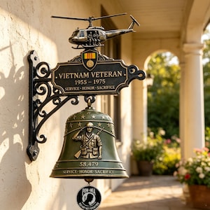 Może przedstawiać: Ścienny metalowy dzwon z helikopterem na górze i tabliczką z napisem VIETNAM VETERAN 1955-1975 SERVICE HONOR SACRIFICE. Zielony dzwon przedstawia salutującego żołnierza, gwiazdy, liczbę 58 479 oraz wiszącą poniżej zawieszkę z napisem POW-MIA.