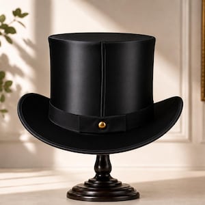 May include: A black top hat with a smooth, satin-like finish and a structured cylindrical crown. The hat features a matching black grosgrain ribbon band around the base, accented with a single, centred, polished gold-tone metal stud.
