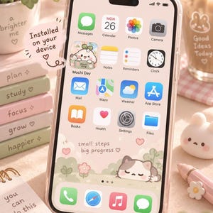 A smartphone displaying a home screen with app icons and a cute cat illustration, surrounded by stacked pastel notebooks and a pen holder.