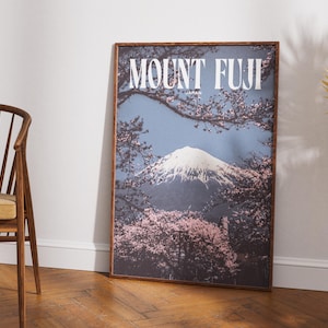 May include: A rectangular framed wall art print featuring a scenic view of Mount Fuji in Japan. The image displays a snow-capped mountain peak framed by blooming pink cherry blossom branches against a muted blue sky, with the text MOUNT FUJI JAPAN.