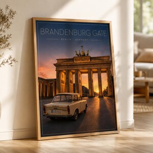 Op de afbeelding: Een ingelijste kunstdruk met de Brandenburger Tor in Berlijn, Duitsland, bij zonsondergang. Een vintage crèmekleurige Trabant-auto staat geparkeerd voor het monument. De tekst luidt BRANDENBURG GATE BERLIN GERMANY in een modern lettertype.