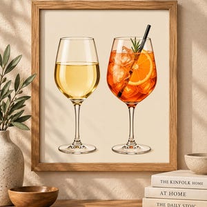 May include: A framed wall art print featuring two stemmed glasses. The left glass contains a pale yellow liquid, while the right glass holds an orange cocktail with ice cubes, a slice of orange, a sprig of rosemary, and a black straw.