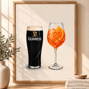 May include: A framed wall art print featuring a dark Guinness stout in a pint glass with its signature white foam head next to a bright orange Aperol spritz in a stemmed wine glass filled with ice cubes and a fresh orange slice garnish.