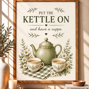 Puede incluir: Una lámina enmarcada con una tetera verde claro y dos tazas a juego sobre un paño de cuadros verdes y blancos. El texto dice: PUT THE KETTLE ON and have a cuppa. El diseño está decorado con flores de margarita blancas y hojas verdes.