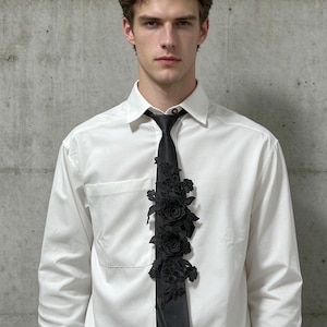 May include: A crisp white long-sleeved button-down shirt paired with a black necktie. The tie features an intricate, three-dimensional black floral lace appliqué running down the centre, showcasing detailed rose and leaf embroidery patterns.