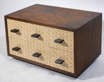 May include: A wooden box with four drawers, each with a geometric pattern and a black handle. The box is made of dark wood with a light wood interior.