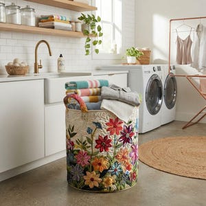 May include: A cylindrical fabric laundry hamper featuring a quilted texture and a vibrant, multi-coloured floral pattern with red, orange, yellow, blue, and purple blossoms. The hamper has two sturdy fabric handles and contains folded towels.