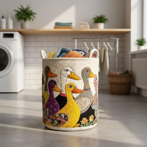 May include: A cylindrical fabric laundry basket featuring a quilted off-white background decorated with a colorful patchwork pattern of various ducks in shades of yellow, purple, green, and grey, complete with two sturdy side handles for carrying.