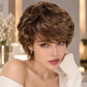 May include: A short, layered brown wig with golden highlights and a textured, wavy finish. The hair is styled with soft volume and side-swept bangs that frame the face. The wig features a natural-looking root colour and multi-tonal brown strands.