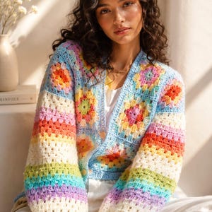 May include: A long-sleeve crochet cardigan featuring a vibrant granny square pattern in shades of blue, pink, yellow, orange, and green. The garment has a V-neckline, light-colored buttons, and sleeves with horizontal stripes in a rainbow color palette.