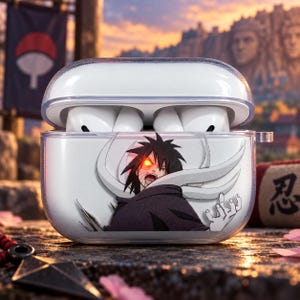 May include: A clear plastic protective case for wireless earbuds featuring a graphic print of a dark-haired character with a glowing red eye and white swirling patterns. The case is open, revealing white earbuds inside the charging compartment.