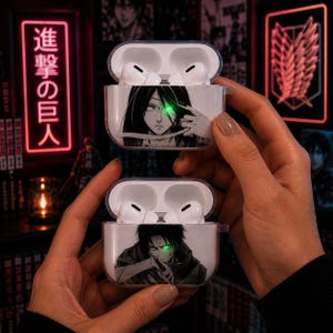May include: Two clear protective cases for wireless earbuds, each featuring a black and white anime character illustration with a glowing green eye effect. The top case depicts a character with long dark hair, and the bottom case shows a character with short dark hair.
