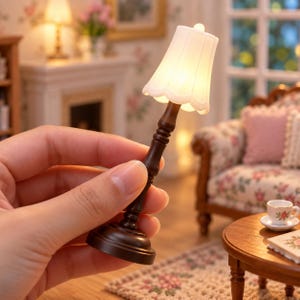 Könnte beinhalten: Eine Miniatur-Tischlampe mit einem dunkelbraunen Holzsockel und einem gewellten, halbtransparenten weißen Lampenschirm, der ein warmes, sanftes Licht ausstrahlt. Die Lampe hat ein schlankes, gedrechseltes Design und einen runden Fuß im Puppenhausmaßstab.