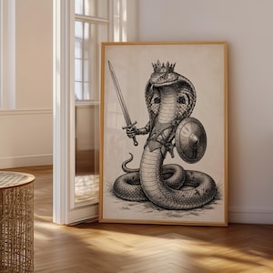 May include: A framed wall art print featuring a black and white ink-style illustration of a cobra wearing a crown and armour. The snake is depicted in an upright position, holding a long sword in one hand and carrying a round shield on its side.