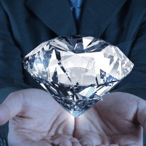 May include: A large, brilliant-cut clear diamond with multiple facets reflecting light. The gemstone is transparent and colorless, displaying sharp geometric edges and a pointed culet at the base, showcasing high clarity and light refraction properties.