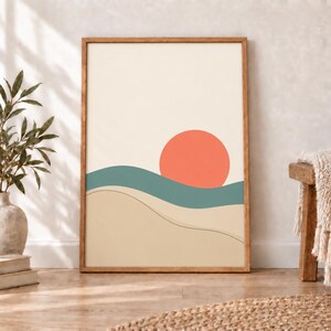 May include: A framed wall art print featuring a minimalist landscape illustration with a large coral-colored circle representing the sun, a teal wavy band representing hills or water, and a beige foreground with a thin black line contour.
