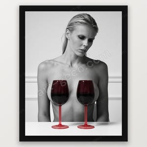 Peut inclure: Une impression photographique en noir et blanc dans un cadre noir représentant une personne aux cheveux blonds attachés, placée derrière deux verres à vin rouges remplis de liquide rouge foncé, devant un mur blanc avec des moulures.