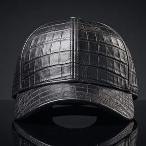May include: A black baseball cap featuring a textured crocodile skin pattern across the entire surface. The cap has a structured crown and a curved brim, with visible stitching details along the panels and a button at the top centre.
