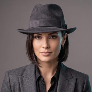 May include: A dark grey fedora hat with a matching band, worn with a dark grey blazer and a black collared shirt. The hat features a structured crown and a medium-width brim, providing a classic silhouette that complements the formal attire.