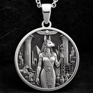 May include: A circular silver-toned pendant featuring a detailed relief of the Egyptian deity Anubis holding an ankh staff. The background depicts ancient Egyptian architecture, including pyramids, columns, and hieroglyphic-style carvings.