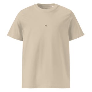 Può includere: Una t-shirt beige a maniche corte con scollo rotondo. Al centro del petto è presente la scritta "roj." stampata in un piccolo carattere serif scuro. Il capo è realizzato in un tessuto a tinta unita con una consistenza liscia.