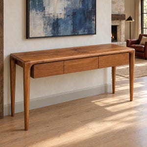 May include: A rectangular wooden console table featuring a smooth, natural grain finish. The table is supported by four tapered legs and includes three horizontal drawers positioned side-by-side along the front apron of the furniture piece.