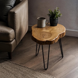 May include: A side table featuring a natural live-edge wood slab top with visible grain patterns, supported by three thin black metal hairpin legs. A light-colored ceramic mug and a small green potted plant sit on the wooden surface.