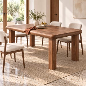 May include: A rectangular wooden dining table with rounded edges and four thick legs, accompanied by four chairs featuring light beige upholstered seats and wooden frames. A white vase with greenery and a stack of plates sit on the table surface.