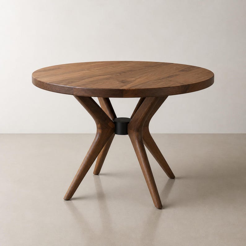 Round solid walnut dining table with a radial wood base and compact black central collar on a warm studio set