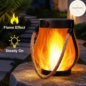 May include: A black lantern with a rope handle and a glowing orange flame effect. The lantern features a black top and base, with text on the left reading Flame Effect and Steady On, and a SimplyKindlyCo logo in the top right corner.