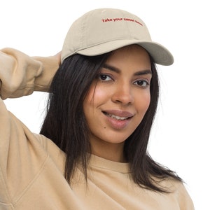 May include: A beige baseball cap with the embroidered text "Take your sweet time" in red. The cap is made of a soft material and has a curved brim. The cap is being worn.