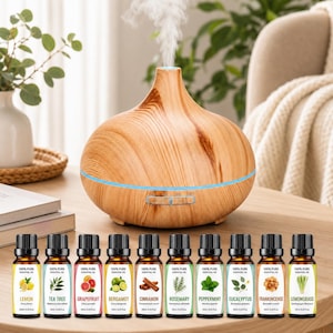 May include: A light wood grain essential oil diffuser with a blue light band and a stream of mist, accompanied by ten small amber glass bottles labelled Lemon, Tea Tree, Grapefruit, Bergamot, Cinnamon, Rosemary, Peppermint, Eucalyptus, Frankincense, and Lemongrass.