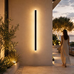 Peut inclure: Une longue applique murale rectangulaire et verticale au fini noir mat, dotée de bandes LED intégrées qui diffusent une lueur chaude et douce contre le mur extérieur, créant un motif d'éclairage linéaire et lumineux sur la surface.