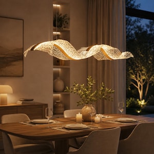 May include: A linear pendant light fixture featuring a long, undulating, wave-like structure with a textured, translucent white surface and gold-toned accents. The fixture is suspended by thin wires and emits a warm, soft glow from within.