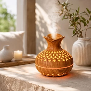 May include: A round, wood-grain finish essential oil diffuser with a cut-out diamond pattern emitting a steady stream of mist. The device features a flared top opening and a glowing orange light band around the centre, resting on a flat surface.