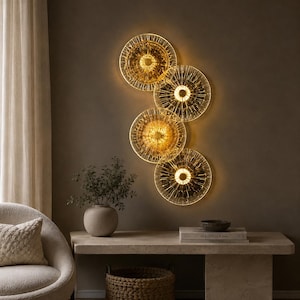 Peut inclure: Une applique murale composée de quatre disques en verre translucide disposés en un motif vertical et superposé. Chaque disque présente un design texturé et radial avec une source lumineuse centrale émettant une lueur dorée et chaude.