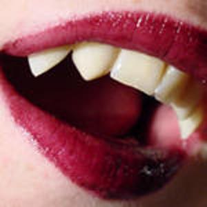 May include: Close-up of a mouth with red lipstick and sharp, pointed teeth. The teeth are a pale yellow color.