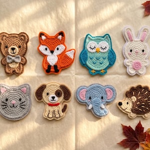 May include: A collection of eight crocheted animal appliques arranged in two rows. The top row features a brown bear, an orange fox, a teal owl, and a white rabbit. The bottom row includes a gray cat, a tan dog, a blue elephant, and a brown hedgehog.