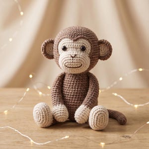May include: A crocheted monkey toy featuring a medium brown body with a lighter beige face, ears, hands, and feet. The monkey has dark brown safety eyes, a stitched nose and mouth, and a long tail, crafted with a visible yarn texture throughout.