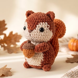 May include: A crocheted squirrel figurine made with dark brown and cream yarn. The squirrel has large black plastic eyes, a small brown stitched nose, and a bushy tail. It is holding a small crocheted acorn with a brown cap and orange body.