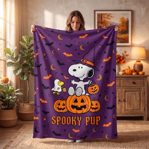 May include: A purple fleece blanket featuring a cartoon dog wearing a witch hat, sitting on a large jack-o'-lantern, with a small ghost character nearby. The design includes orange pumpkins, black bats, yellow crescent moons, and the text SPOOKY PUP.