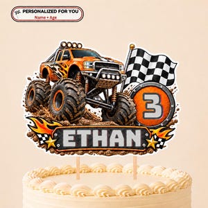 May include: A cake topper featuring an orange monster truck with flame decals, a black and white checkered flag, and a circular emblem with the number 3. A rectangular plaque at the bottom displays the name ETHAN in bold letters with flames.