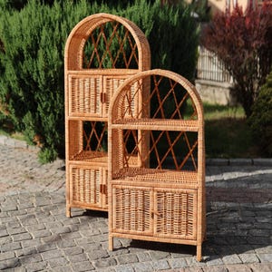 Puede incluir: Dos estanterías de mimbre arqueadas con acabado en color marrón claro natural. Cada unidad cuenta con un estante superior abierto con respaldo de celosía en forma de diamante y una sección de armario inferior con dos puertas.