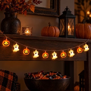 May include: A string of Halloween LED lights featuring alternating orange jack-o'-lanterns and white ghosts. The illuminated figures are connected by a thin wire, creating a festive glow. Each pumpkin has a carved face, and each ghost has a smiling expression.