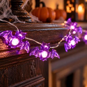 Könnte beinhalten: Eine Lichterkette mit violetten, fledermausförmigen LED-Leuchten, die durch einen dünnen Draht verbunden sind. Jede durchscheinende violette Fledermaus hat in der Mitte ein helles weißes Licht, das entlang der Lichterkette leuchtet.