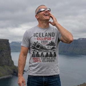 May include: A heather gray t-shirt featuring the text ICELAND ECLIPSE 2026 12 AUGUST above a graphic of clouds and six figures wearing eclipse glasses. Below the graphic, the text reads 100% TOTALITY. 100% CLOUDY. The shirt has a crew neckline.