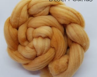 May include: A close-up of a bundle of soft, orange wool roving. The wool is arranged in a circular shape and has a slightly textured appearance. The text "Desert Sands" is visible in the upper right corner of the image.