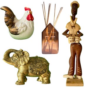 May include: A collection of decorative items including a white and brown ceramic rooster, a house-shaped glass diffuser with reeds, a gold-toned elephant figurine with ornate detailing, and a tall wooden sculpture of a person playing drums.