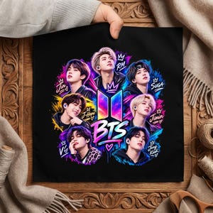 May include: A black fabric square featuring a vibrant graphic of the seven members of the music group BTS. The design includes colorful paint splatters, the BTS logo, and the names Jin, RM, Suga, J-Hope, Jimin, V, and Jung Kook in stylized text.
